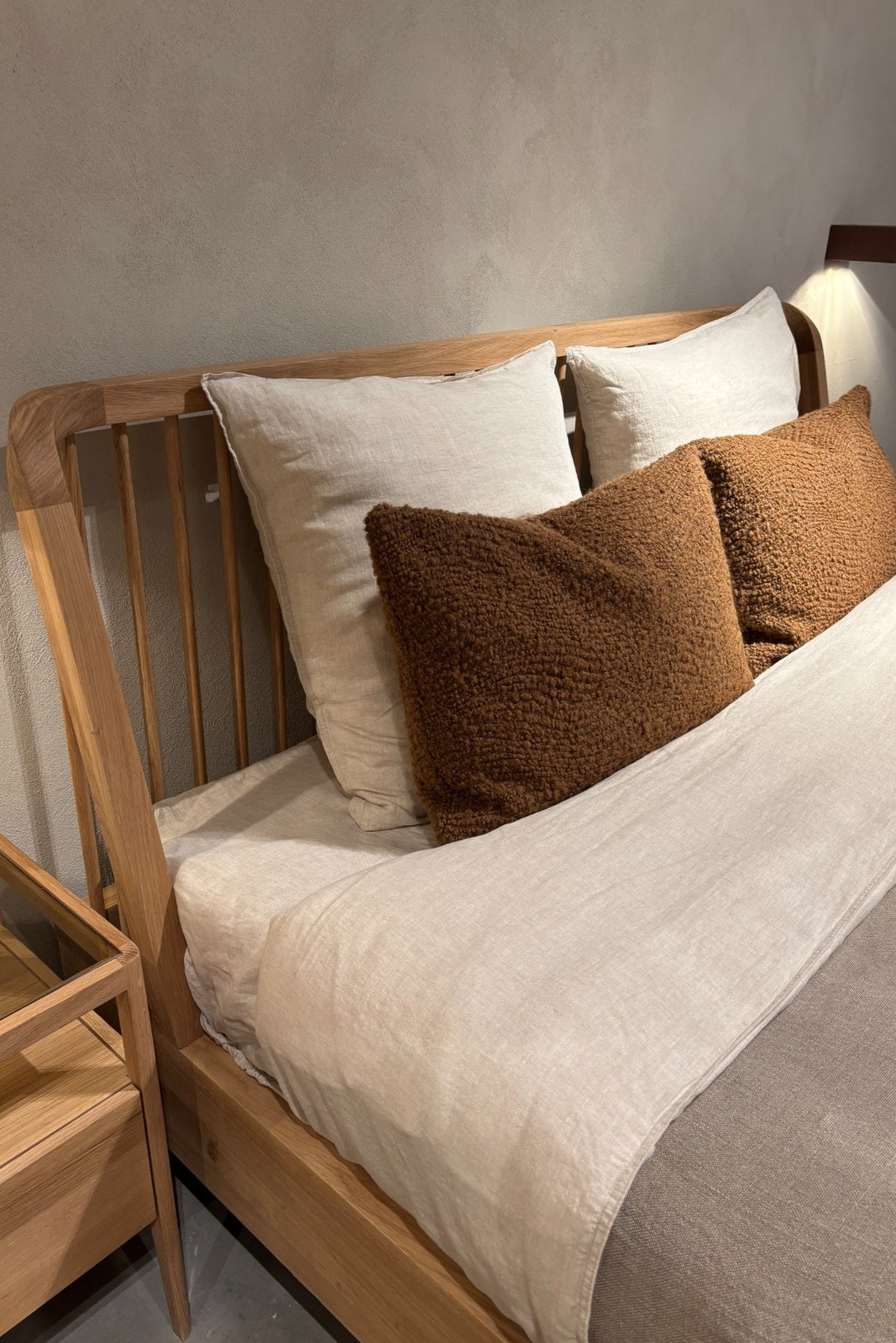 Natural wood bed frame with white linen bedding and pillows in a Scandinavian inspired bedroom design