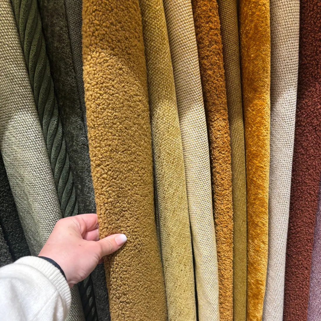 Close-up of hand selecting colourful fabric samples for curated interiors.