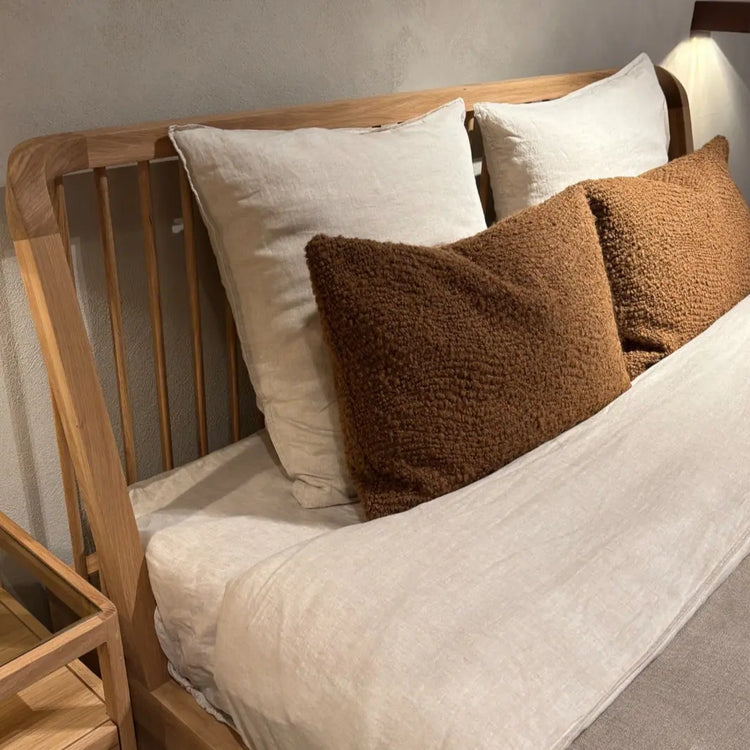 Natural wood bed frame with white linen bedding and pillows in a Scandinavian inspired bedroom design.